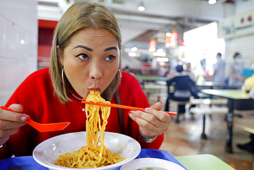 Young woman eating at traditional Asian food stall in Singapore Food Trail hawker center, Singapore, Southeast Asia, Asia