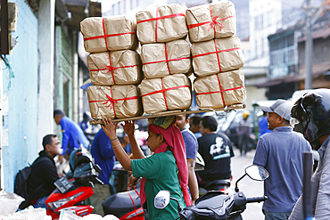 Daily worker at traditional food market. Woman carrying heavy bags with on her head. Surabaya. Indonesia.