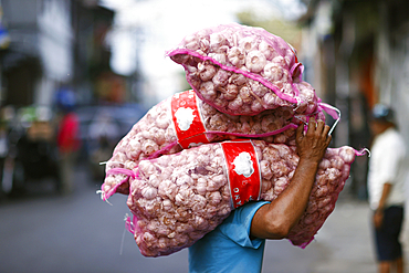 Daily worker at traditional food market, man carrying heavy bags with garlic on his head, Surabaya, Java, Indonesia, South East Asia, Asia