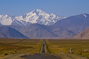 Country road leading to snow covered mountains, Karakul, Tajikistan, Central Asia