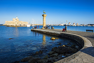 The old Agios Nikolaos fortress and lighthouse in Mandraki Harbour with deer statue in foreground, Rhodes Town, Rhodes, Dodecanese Islands, Greek Islands, Greece, Europe