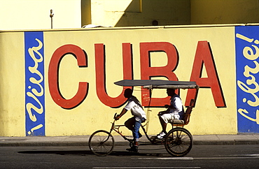 Bicycle taxi passing Viva Cuba wall mural, Havana, Cuba, West Indies, Central America