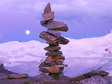 A cairn of balanced rocks with a moon rise and mountains in background, Gornergrat, Zermatt, Valais, Switzerland, Europe