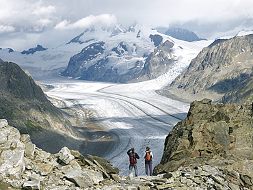 Two hikers looking at the Aletsch glacier, Aletsch, Goms Region, Switzerland, Europe