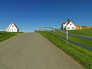 Road lined with fence and white clapboard home in the town of Perce, Gaspesie, Quebec, Canada, North America