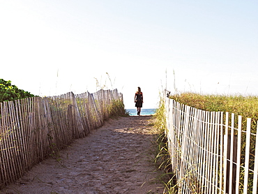 Woman looking out to sea from path leading to beach with wooden fence, South Beach, Miami, Florida, United States of America, North America