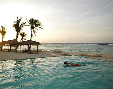 Male swimmer doing laps in an infinity pool located by the beach by the sea at sunrise, Mayan Riviera, Akumal, Yucatan, Quintana Roo, Mexico, North America