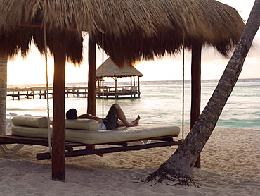 Man lying on swinging daybed under palapa watching sunrise, Mayan Riviera, Akumal, Yucatan, Quintana Roo, Mexico, North America