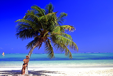 Man relaxing against palm tree with Caribbean Sea as background, Bavaro Beach, Punta Cana, Dominican Republic, West Indies, Caribbean, Central America