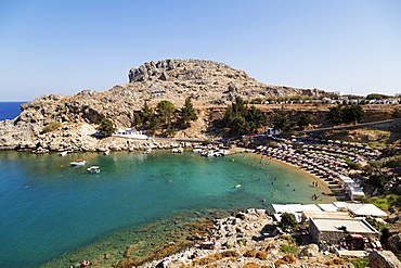 Sun shades line the beach at St. Paul's Bay on a sunny day in Lindos on Rhodes, Dodecanese, Greek Islands, Greece, Europe