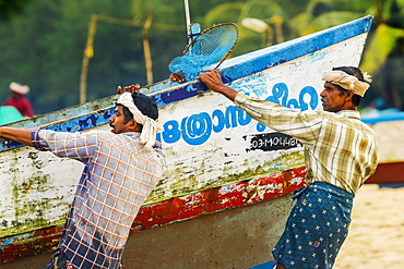 Fishermen pulling heavy old boat on to shore at busy, popular Marari Beach, Mararikulam, Alappuzha (Alleppey), Kerala, India, Asia