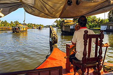 Captain on phone and steering houseboat through the backwaters on a popular backwater cruise, Alappuzha (Alleppey), Kerala, India, Asia