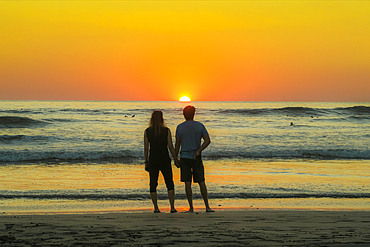 Couple hold hands on Guiones Beach where people gather to surf and watch at sunset, Playa Guiones, Nosara, Guanacaste, Costa Rica, Central America