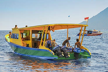 Dive boat with young foreign tourists and crew off coral fringed holiday and scuba island, Bunaken, North Sulawesi, Indonesia, Southeast Asia, Asia