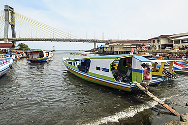 Covered ferry boats in Manado port with the Soekarno Bridge beyond in provincial capital of Sulawesi's far north, Manado, North Sulawesi, Indonesia, Southeast Asia, Asia