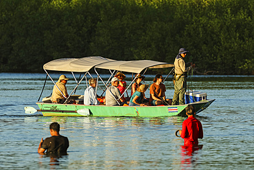 Tourists on a boat trip through the mangrove fringed Nosara River estuary, with locals handline fishing. Boca Nosara, Nosara, Guanacaste, Costa Rica