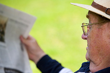 A relaxing senior citizen sitting in the garden reading a newspaper