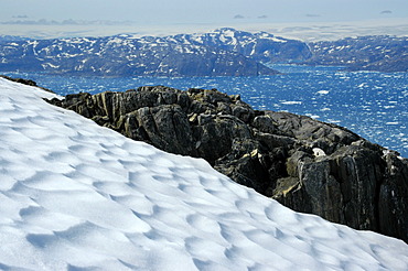 Wide open view over a snow field and rocks to icebergs in Sermilik Fjord Eastgreenland