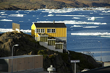 Yellow house above fjord with ice-pack Ammassalik Eastgreenland