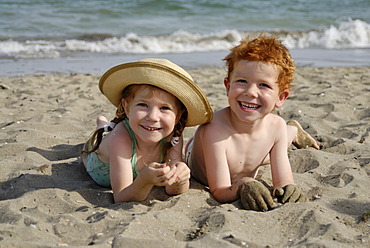 Two children are lying on a sandy beach at the sea