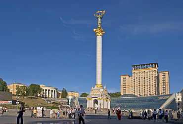 Ukraine Kiev Place of Independence with column of independence and hotel Kiev middle side glasfront of shopping center Globus II Zovtnevyj-palace left side people in front of column of Independence sitting shopping talking blue sky 2004