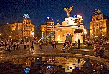 Ukraine Kiev Place of Independence people tourists visitors sit on the place with view to the PecersÂ´kyi gate with archangel Michael and fountain with water iluminated place with historical buildings of sowjetic realismn architectur national holiday 2004