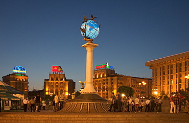 Ukraine Kiev Place of Independence people tourists visitors sit on the place with view to building of neoclassic house of labor union right and column with the world globe iluminated place with historical buildings of sowjetic realismn architectur nationa