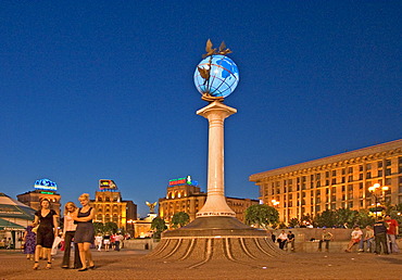 Ukraine Kiev Place of Independence people tourists visitors sit on the place with view to building of neoclassic house of labor union right and column with the world globe iluminated place with historical buildings of sowjetic realismn architectur nationa