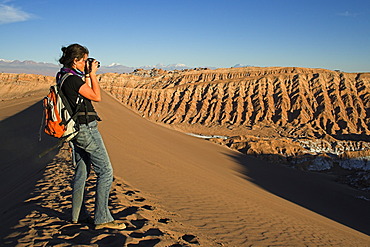 Woman with a camera on a sand dune in the Moon Valley (Valle de la luna), Atacama desert, northern Chile, South America