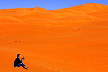 Woman sitting in the desert sand with a camera in her hand, Ubari Sand Sea, Sahara, Libya, Africa