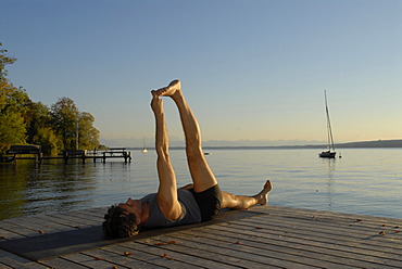 Man doing yoga on a wooden pier by a lake