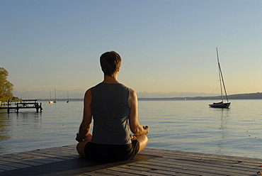 Man doing yoga on a wooden pier by a lake