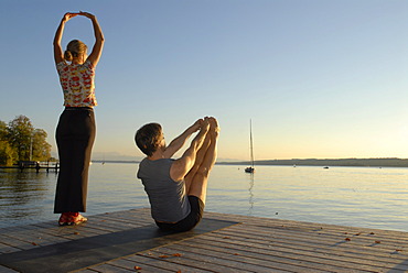 Woman and man doing yoga on a wooden pier by a lake