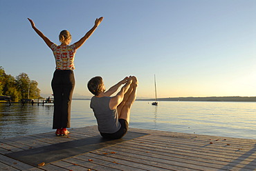 Woman and man doing yoga on a wooden pier by a lake