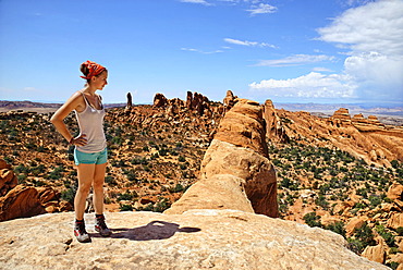 Hiker standing on Double O Arch with a view over Devil's Garden, with its sandstone formations created by erosion, Arches-Nationalpark, near Moab, Utah, United States