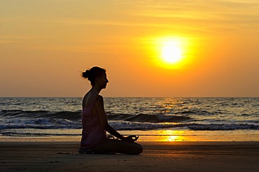 Woman meditating on a beach at sunset, Kerala, India