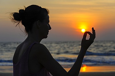 Woman meditating on a beach at sunset, Kerala, India