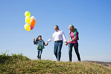 Girls holding balloons in her hand while walking with her grandparents across a meadow