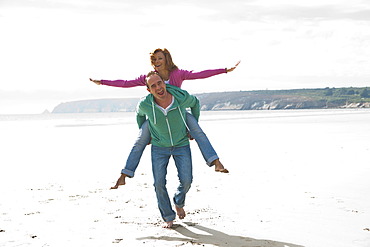 Man carrying a woman piggyback on a beach