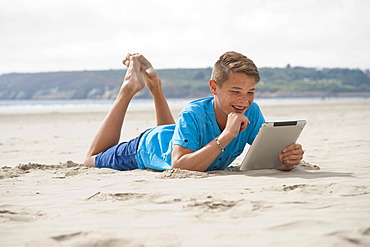 Teenager lying with an iPad on a beach