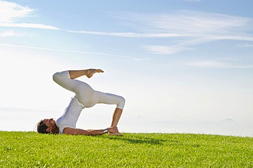 Young woman practising Hatha yoga, here a variation of halasana, supta konasana, variation of plough