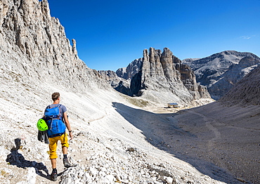 Hiker descending from the Santner via ferrata to the Gartl hut, Rifugio Re Alberto, at the back climbing cliffs, Vajolett towers, Rosengarten group, Dolomites, South Tyrol, Trentino-Alto Adige, Italy, Europe