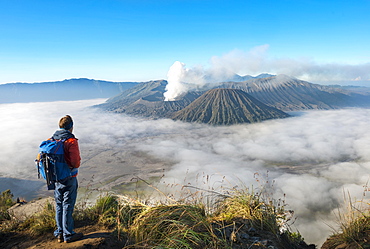 Young man in front of volcanic landscape, view in Tengger Caldera, smoking volcano Gunung Bromo, in front Mt. Batok, behind Mt. Kursi, Mt. Gunung Semeru, National Park Bromo-Tengger-Semeru, Java, Indonesia, Asia