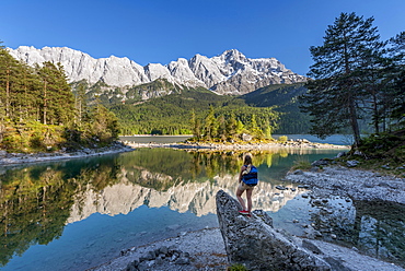 Hiker stands on rocks, looks into the distance, Lake Eibsee lake and Zugspitze, Wetterstein range, near Grainau, Upper Bavaria, Bavaria, Germany, Europe