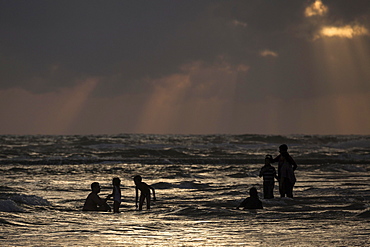 People in backlight in water, rays of sunlight, dark clouds over sea, Beruwela, Western Province, Sri Lanka, Asia