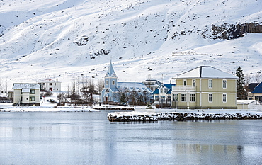 View of the blue church Seyoisfjaroarkirkja in the village Seyoisfjorour with snow, reflection in the lake Fjaroara, Austurland, East Iceland, Iceland, Europe