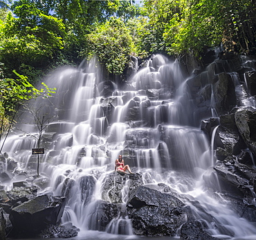 Woman sitting on rock, waterfall, Air Terjun Kanto Lampo, near Ubud, Bali, Indonesia, Asia