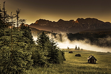 Small cabin on mountain meadow at forest edge, Geroldsee in the background Karwendel Mountains at sunrise, Kaltenbrunn, Upper Bavaria, Germany, Europe