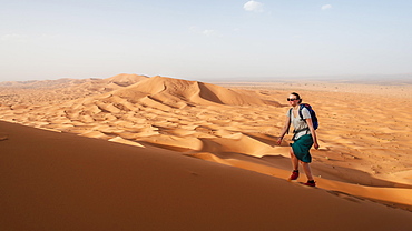 Female hiker is running on a red sand dune in the desert, dune landscape Erg Chebbi, Merzouga, Sahara, Morocco, Africa