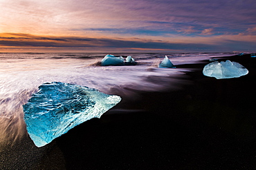 Chunks of ice on black lava sand beach at sunrise, lake Jokulsarlon, Vik, Iceland, Europe